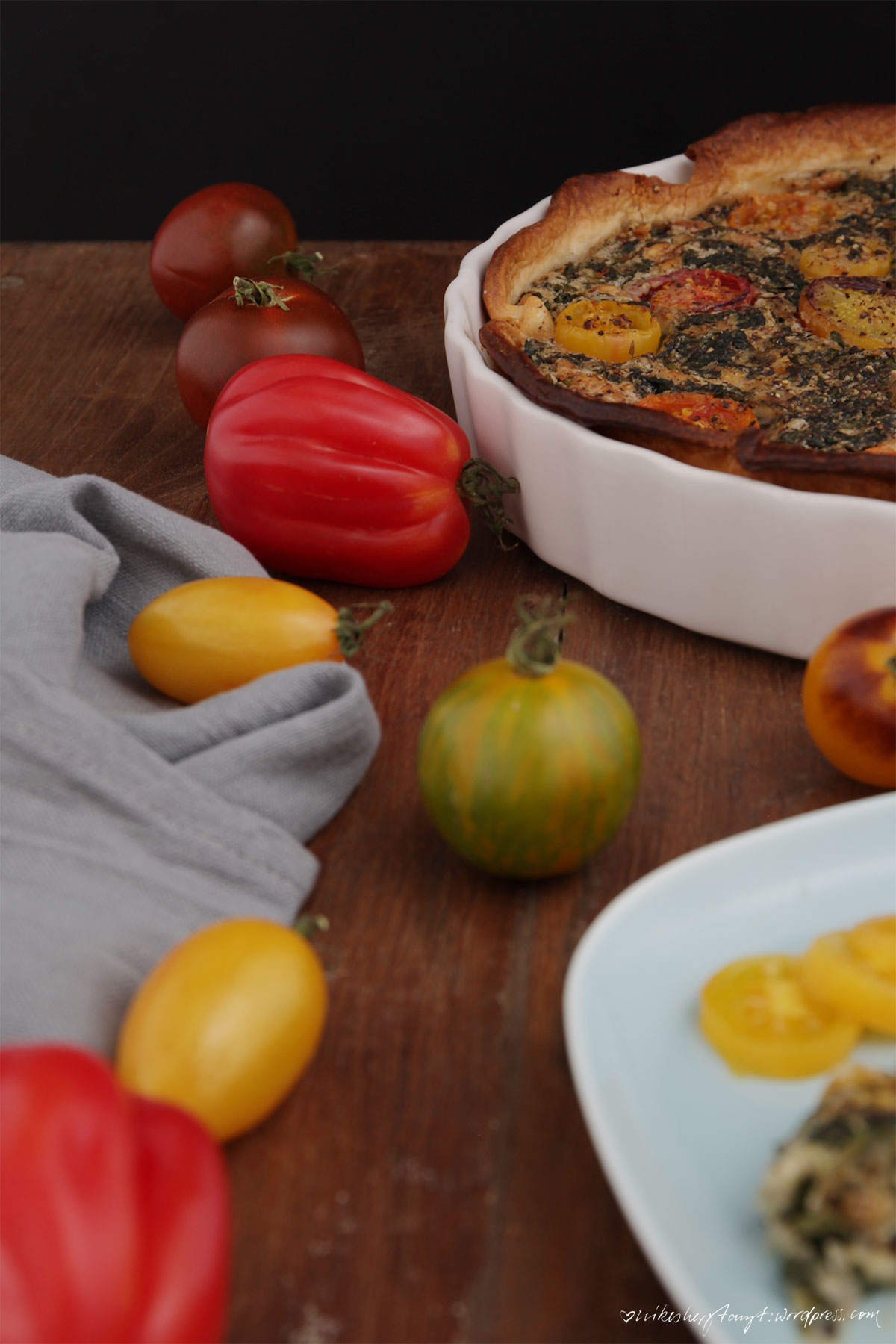 vegane spinat quiche mit pinienkernen und bunten tomaten in weißer form auf holz, nikesherztanzt